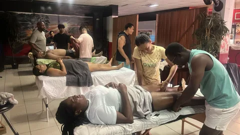 Cursisten oefenen sportmassage op meerdere behandeltafels tegelijk
