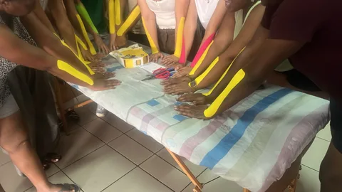 Cursisten met kinesiotape op hun onderarmen rond een behandeltafel
